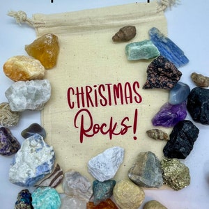 May include: A white drawstring bag filled with 25 assorted rocks and crystals. The bag has the text "CHRISTMAS Rocks!" printed in red on the front.