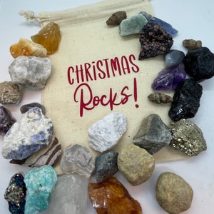 May include: A white canvas bag filled with a variety of rocks and crystals. The bag has the text "Christmas Rocks!" printed on it in red.