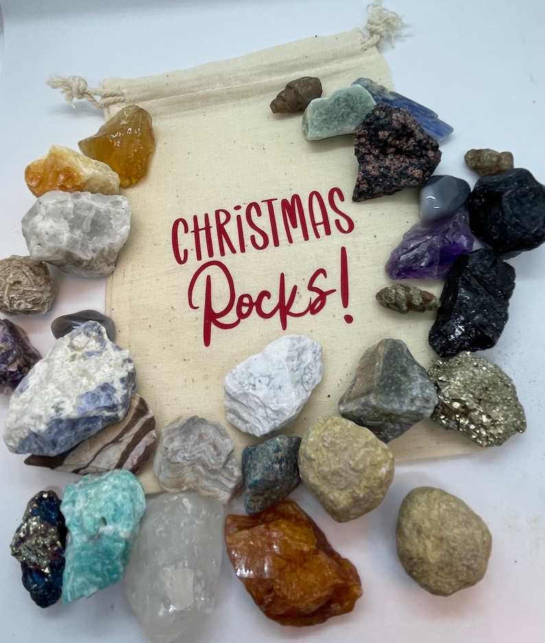 May include: A white canvas bag filled with a variety of rocks and crystals. The bag has the text "Christmas Rocks!" printed on it in red.