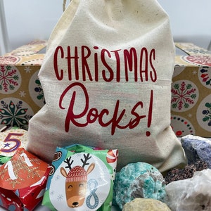 May include: A white canvas bag with red text that says "Christmas Rocks!" The bag is filled with wrapped gifts and colorful rocks.