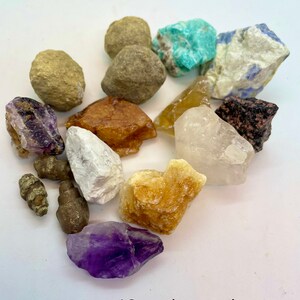 May include: A 12 pack sample of various crystals and stones, including amethyst, citrine, clear quartz, and turquoise. The stones are arranged on a white surface.