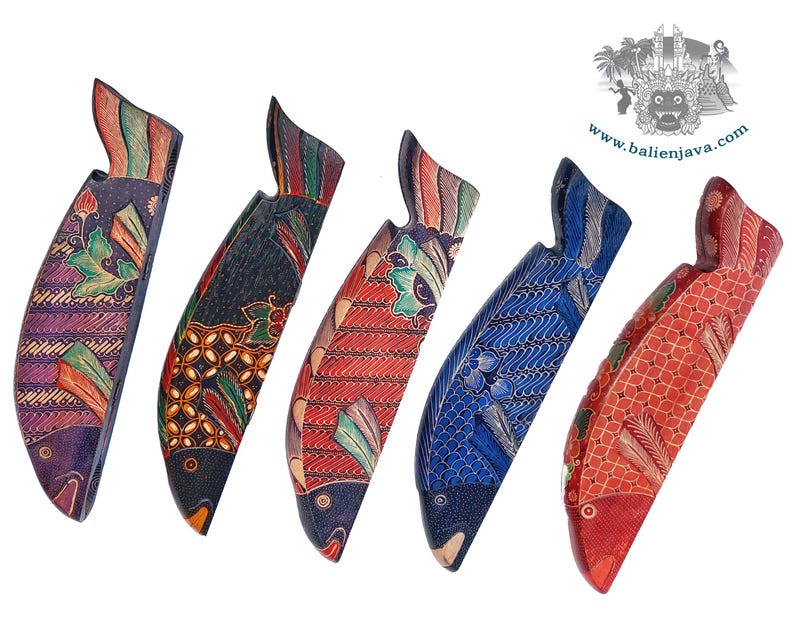 Puede incluir: Cinco figuras de peces de madera tallada dispuestas en fila, cada una con distintos patrones pintados a mano de estilo batik en morado, negro, rojo y azul. Los peces est&aacute;n orientados verticalmente con escamas y aletas detalladas. El texto dice www.balienjava.com.