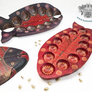 Puede incluir: Tres tableros de juego de madera con forma de pez y dise&ntilde;o plegable con bisagras. Un tablero es rojo con hendiduras circulares, otro es morado oscuro con hendiduras similares y el tercero es un tablero cerrado con patrones pintados complejos.