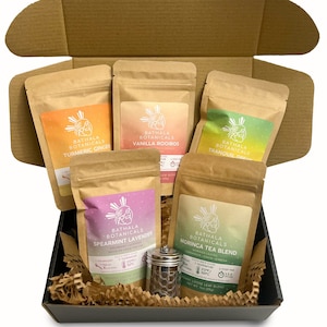 May include: A gift box filled with six different types of loose leaf tea in brown paper bags. The tea flavors are Turmeric Ginger, Vanilla Rooibos, Tranquil Dream, Spearmint Lavender, and Moringa Tea Blend. The box also includes a silver tea infuser.