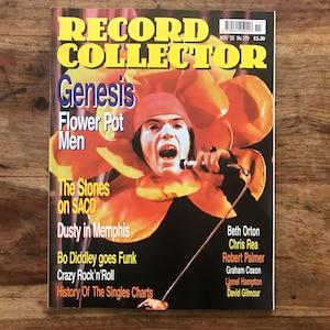 May include: A magazine cover featuring a photo of a man wearing a large flower pot costume. The magazine is titled "Record Collector" and the cover story is about the band Genesis. The cover also includes a list of other articles, including "The Stones on SACD", "Dusty in Memphis", "Bo Diddley goes Funk", "Crazy Rock'n'Roll", and "History Of The Singles Charts".