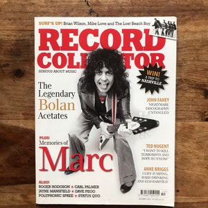 Op de afbeelding: Een tijdschriftcover met een foto van Marc Bolan, een Britse zanger-songwriter, die gitaar speelt. Het tijdschrift is getiteld "Record Collector: Serious About Music" en bevat de tekst "The Legendary Bolan Acetates" en "Memories of Marc".