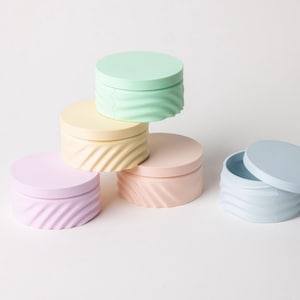Può includere: Cinque contenitori rotondi di colore pastello con coperchi. I contenitori sono impilati a forma di piramide. I colori sono azzurro chiaro, rosa chiaro, pesca chiaro, giallo chiaro e verde chiaro.