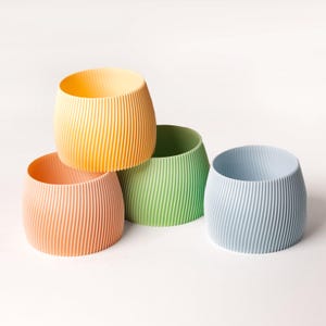 Peut inclure: Quatre tasses cylindriques côtelées de couleurs vives dans des tons de jaune, vert, bleu clair et pêche.