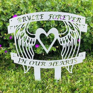 May include: White metal memorial garden stake with a heart and angel wings. The stake has the text "Brylee Forever" and "In Our Hearts".