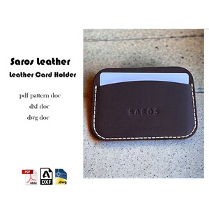 May include: A brown leather card holder with a white stitch detail and the word "SAROS" embossed on the front. The card holder is on a light brown surface.