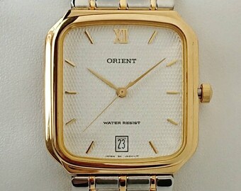 May include: A gold and silver two-tone Orient watch with a square face and a white dial. The watch has a date window at the 3 o'clock position and says "Water Resist" on the dial.