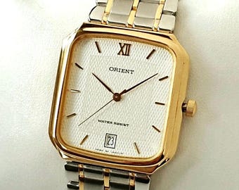 May include: An Orient wristwatch with a square gold-tone case and a textured white dial. The watch features gold-tone hands, a Roman numeral at the twelve o'clock position, a date window at six o'clock, and a two-tone silver and gold metal link band.