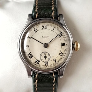May include: A silver wristwatch with a white face and black hands. The watch has Roman numeral hour markers and a small second hand dial. The watch is on a green leather strap.