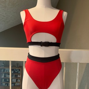 May include: Red and black high-waisted bikini with a cut-out detail and a buckle on the top.