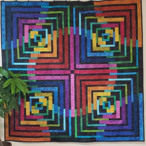 May include: A colorful quilt with a geometric pattern of squares and rectangles. The quilt is made up of various shades of blue, green, red, orange, yellow, and purple. The quilt is hanging on a wall.