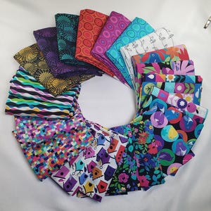 May include: A circular arrangement of folded fabric squares with various colorful patterns. Designs include geometric shapes, floral prints, birdhouses, and abstract lines. The fabrics feature a range of colors, including purple, teal, orange, and pink.