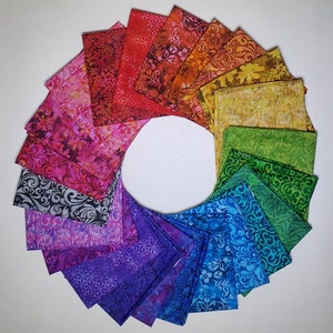 May include: A circular arrangement of colorful fabric squares, showcasing a spectrum of hues from red to purple. Each square features a unique floral or patterned design. The fabrics are arranged in a rainbow pattern, creating a visually appealing display.