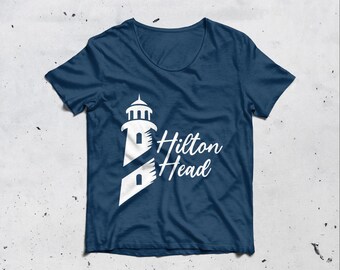 May include: A navy blue t-shirt with a white lighthouse graphic and the words "Hilton Head". The lighthouse design is modern and clean. The shirt has a crew neck. The text is in a script font. The t-shirt is a classic style.