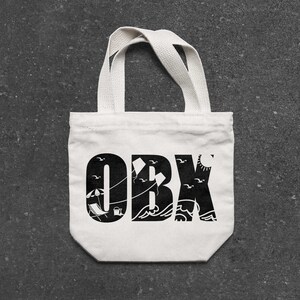 May include: White canvas tote bag with black text that says "OBX" with a beach scene design including an umbrella, beach chairs, and seagulls.