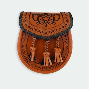 May include: A brown leather sporran with a Celtic knot design and black stitching. The sporran has three tassels.