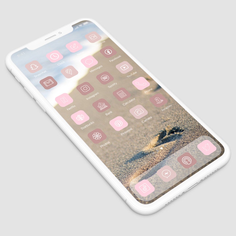 May include: A white smartphone with a pink and white app icon design. The phone's background is a sandy beach with a single footprint.
