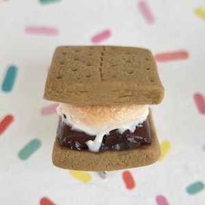 May include: A miniature s'more with a graham cracker base, a layer of chocolate, and a white marshmallow on top.