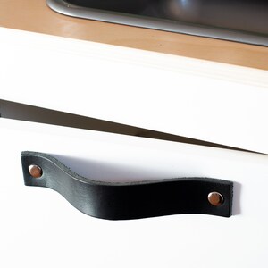 May include: A white cabinet with a black leather handle. The handle has two silver rivets.