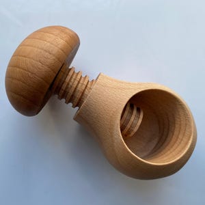 Könnte beinhalten: Ein hellbrauner Nussknacker aus Holz mit einem abgerundeten Griff und einem Gewindeschraubmechanismus, der in eine hohle, birnenförmige Basis greift. Die natürliche Holzmaserung ist auf der glatten, polierten Oberfläche dieses Werkzeugs sichtbar.