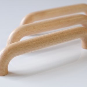 May include: Three wooden cabinet pulls with a rounded, arched shape. The pulls are made of light wood and have a smooth, natural finish.