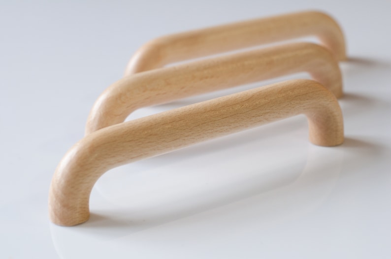 May include: Three wooden cabinet pulls with a rounded, arched shape. The pulls are made of light wood and have a smooth, natural finish.