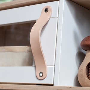 May include: White cabinet with a glass door and a leather handle. A wooden nutcracker shaped like a mushroom is on the shelf below the cabinet.