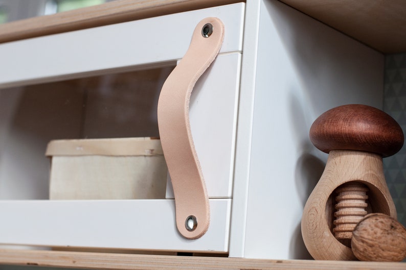 May include: White cabinet with a glass door and a leather handle. A wooden nutcracker shaped like a mushroom is on the shelf below the cabinet.