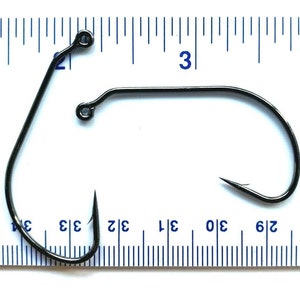 May include: A black fishing hook with a swivel, measured against a ruler. The hook is approximately 3 inches long.