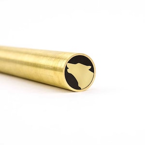 Puede incluir: Un blank de bolígrafo de latón con un diseño de cabeza de lobo negro y dorado.