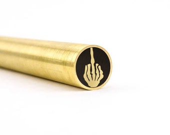 May include: A brass pen with a black and gold skeleton hand giving the middle finger.