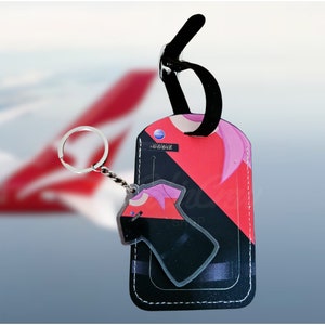 May include: A black leather luggage tag with a red and black design. The tag has a loop for attaching to a suitcase and a smaller keychain with a black and red design.