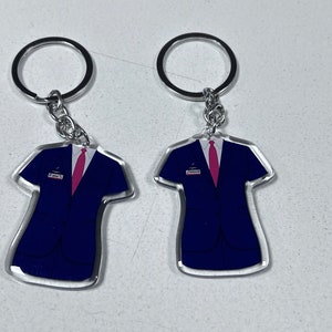 May include: Two clear acrylic keychains shaped like a suit jacket with a pink tie. The keychains are attached to silver key rings.