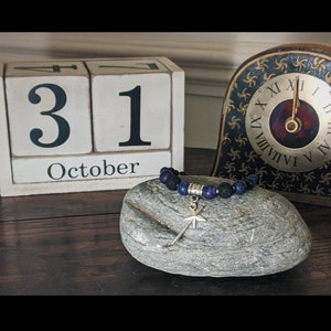 May include: A wooden block calendar with the date October 31st, a rock with a beaded bracelet with a star charm, and a clock with Roman numerals.