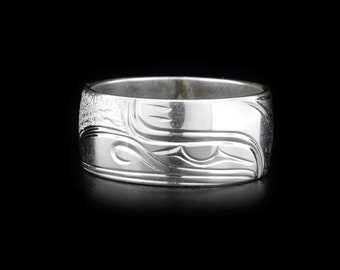 May include: A wide silver band ring featuring a polished finish and intricate, recessed engraved lines that form abstract, flowing shapes across the outer surface. The metal has a reflective quality with a smooth, rounded edge profile.