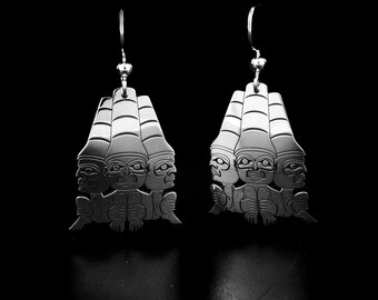 May include: A pair of silver earrings with a design of three faces stacked on top of each other. The faces are stylized and have a geometric look.