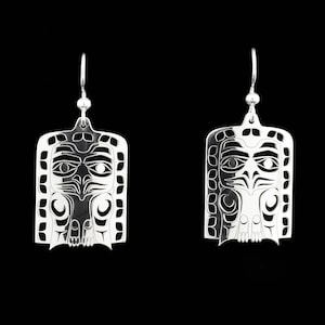 Peut inclure: Une paire de boucles d'oreilles en argent avec un motif découpé détaillé d'un visage. Les boucles d'oreilles sont de forme rectangulaire et ont un style amérindien traditionnel.