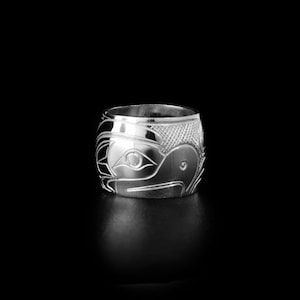 May include: A silver ring featuring an intricate carving of a bird's face. The ring is wide and has a polished finish.