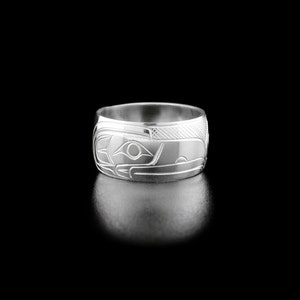 May include: A silver ring with an intricate design of a bird's face. The ring is wide and has a polished finish.