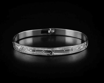 May include: A silver bangle bracelet with a detailed etched design. The design features a repeating pattern of stylized figures.
