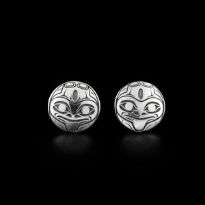 Può includere: Un paio di orecchini d'argento con un design rotondo e un viso stilizzato. Gli orecchini sono realizzati in argento sterling e sono un accessorio unico ed elegante.