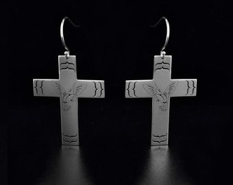 May include: A pair of silver cross earrings with a hummingbird design. The earrings are dangle style and have a hook closure.