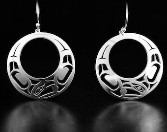 May include: A pair of silver earrings with a circular design featuring a stylized animal figure. The earrings are made of sterling silver and have a polished finish.