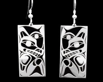 May include: A pair of silver dangle earrings with a black and white design of a wolf's face. The earrings are rectangular in shape and have a simple hook closure.
