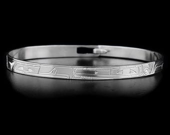 May include: A silver bangle bracelet with an intricate engraved design. The design features geometric shapes and lines.