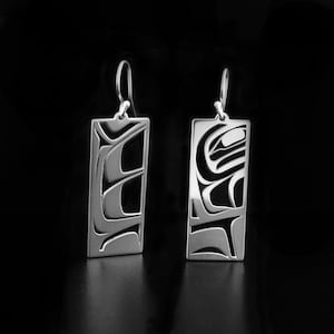 Peut inclure: Une paire de boucles d'oreilles rectangulaires argentées avec un motif abstrait stylisé. Les boucles d'oreilles sont dotées d'une fermeture à crochet et d'un motif découpé avec des accents noirs, sur fond noir. Le design semble inspiré de l'art amérindien.